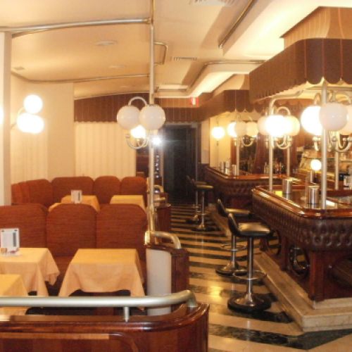 Interior de la cafetería con butacas a la izquierda, barra a la derecha y puerta al fondo